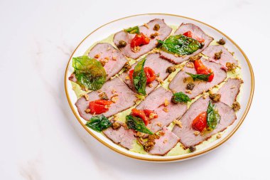 Çok güzel düzenlenmiş bir tabakta canlı domatesler ve taze otlarla süslenmiş taze biftek dilimleri yer alıyor. Renkli bileşenler sunum ve lezzet profilini geliştirir.