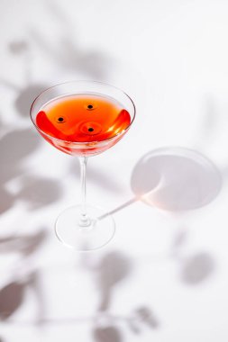 Üzerinde kirazlar yüzen canlı bir kokteyl zarif bir şekilde şık bir bardakta durur. Camdan dökülen gölgeler, arka planda küçük bir etki yaratıyor..