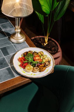 Bitkilerle süslenmiş kabak ve patlıcan da dahil olmak üzere canlı bir sebze çeşidi güzel bir tabakta duruyor. Sıcak ortam, yumuşak ışıklandırmayla gelişir..