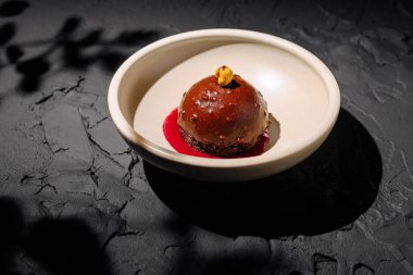 Zengin bir çikolatalı tatlı canlı böğürtlen sosuyla çevrili dokulu bir tabağın üzerine oturur. Bir tutam fındık bir tutam zarafet ekler ve enfes bir mutfak sunumu yaratır..