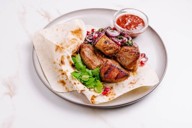 Sulu ızgara kebaplar taze kişniş ve soğan garnitürlü yumuşak bir ekmeğin üzerine konur. Lezzetli ve lezzetli bir yemek seçeneği için bir kase baharatlı sos eşliğinde..