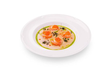 Narin somon balığı dilimleri canlı narenciye sosuyla kaplanmış ve mikro yeşilliklerle süslenmiş beyaz bir tabakta ustalıkla düzenlenir. Bu yemek zarif bir sunum ve lezzet sunar..