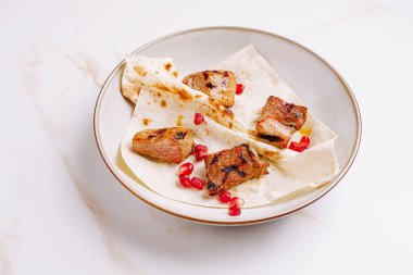 Yumuşak ızgara et parçaları yumuşak düz ekmeğin üzerinde zarif bir şekilde düzenlenir ve tatlı bir dokunuş için canlı nar çekirdekleri eşliğinde. Bu yemek, dokuların ve tatların bir karışımını sergiliyor..
