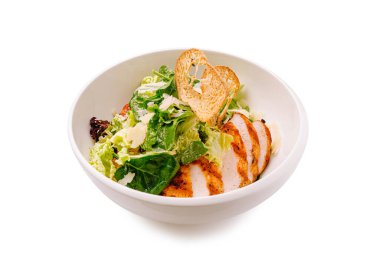 Bir kase taze marul yatağının üzerinde kızarmış tavuk dilimleri içeriyor, gevrek yeşilliklerle tamamlanmış ve kızarmış ekmekle süslenmiş. Yemek çekici ve sağlıklı görünüyor, öğle yemeği için uygun..