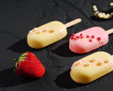 Çilek ve vanilya aromalı koyu bir yüzeye üç renkli dondurma sergileniyor. Taze bir çilek zengin kompozisyona canlı bir dokunuş ekler..