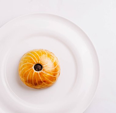 Güzelce hazırlanmış bir hamur işi, temiz beyaz bir tabağa odaklanmış ve onun karmaşık altın-kahverengi tasarımını vurguluyor. Odaklanma, bu aşçılık yaratılış sanatını vurguluyor..