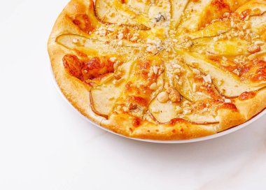 Taze armut dilimleri, erimiş peynir ve ezilmiş fındık ile kaplı güzel işlenmiş bir düz ekmek beyaz bir tabakta servis edilir. Yemek davetkar ve eğlenmeye hazır görünüyor..