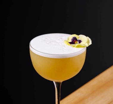 Güzel işlenmiş bir kokteyl köpüklü sarı bir renk ve küçük yenilebilir bir çiçek içerir. İçki koyu bir arka plana göre ayarlanmış, entelektüellik yayılıyor..