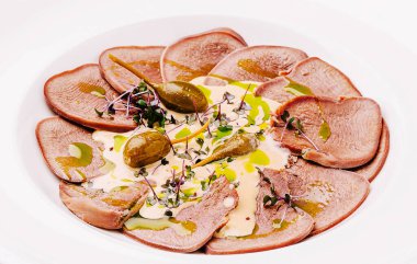 Keskin bir sos serpiştirilmiş, kapari ve taze otlarla süslenmiş, beyaz bir tabakta ince ince ince kesilmiş etler, zevk için iştah açıcı bir yemek takımı oluşturur..