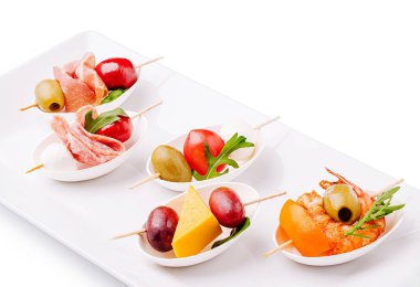 Dilimlenmiş etler, zeytinler, kiraz domatesleri ve peynirden oluşan beyaz bir tabakta sunulan tapaların çeşitliliği. Sıradan bir yemek ortamında paylaşmak için mükemmel..