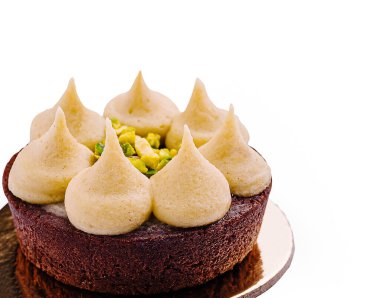 Çürümüş çikolatalı pasta, kremalı krema zirveleri ve ezilmiş şam fıstığı serpiştirilmiş altın bir zeminde duruyor. Sunum, zengin dokularını ve lezzetlerini vurguluyor.