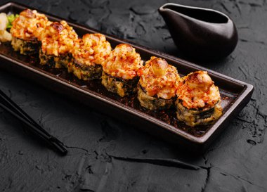 Üzerine ızgara deniz ürünleri konmuş suşi ruloları zarif, koyu bir tabakta otururlar. Soya sosu ve yemek çubuklarının eşlik ettiği bu yemek, mutfağın yaratıcılığını ve lezzetlerini ön plana çıkarıyor..