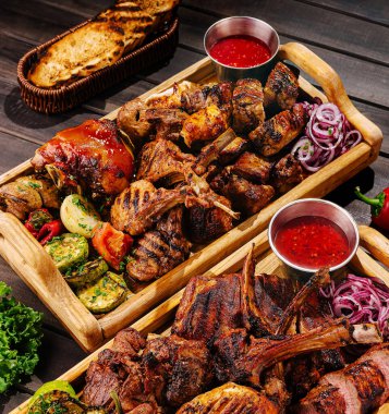 Kaburga, tavuk ve biftek de dahil olmak üzere leziz et parçaları renkli sebzeler ve soslarla birlikte ahşap bir tabakta sunuluyor..
