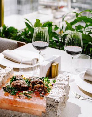 Lüks bir yemek deneyimi, yanında kırmızı şarap kadehleriyle tuz bloğunda sunulan bir gurme yemeği içerir. Yeşillik zarif masa düzenini sarar.