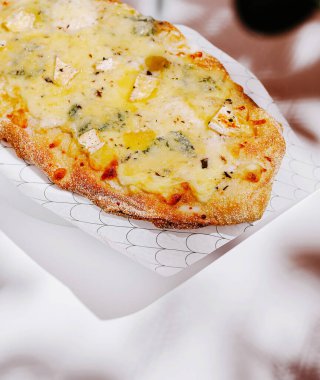 Sıcak bir lokantada eritilmiş peynirli, otlu ve zeytinli taze pişmiş bir ekmek servis ediliyor. Koku havayı dolduruyor, müşterileri bu lezzetli yemeğin tadını çıkarmaya davet ediyor..