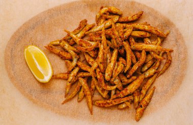 Büyük bir tabakta düzgünce hazırlanmış, yanında limon dilimi ile birlikte kızarmış balık. Sıradan bir yemek sırasında paylaşmak ya da atıştırmalık olarak keyif almak için mükemmel..