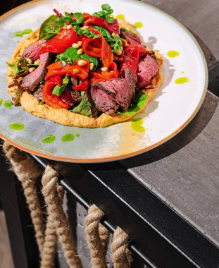 Renkli sebzelerle süslenmiş lezzetli bir ızgara et tabağında çok güzel duruyor. Canlı yeşiller ve kırmızılar leziz eti ön plana çıkararak, davetkar bir aşçılık gösterisi yaratıyor..