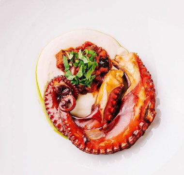 Güzel kaplanmış ahtapot çanağı yumuşak dokunaçlar sergiliyor. Yumuşak, kremsi bir taban üzerinde lezzetli bir sos ile eşleştirilmiş. Taze otlar yemeği süslüyor, görsel cazibesini arttırıyor..