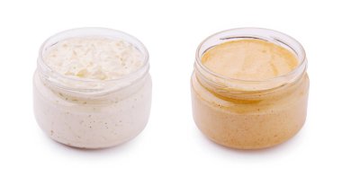 Farklı kremalı soslar içeren iki küçük cam kavanoz beyaz arka planda yan yana oturur. Sol kavanozda otlu beyaz sos, sağ kavanozda ise pürüzsüz bej sosu var..