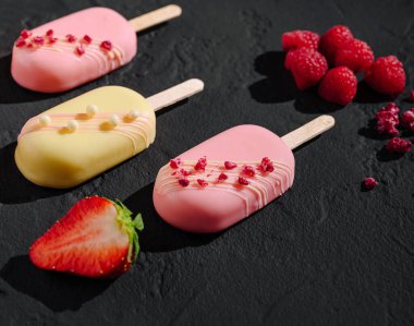 Yakınlarda taze çilek ve ahududu bulunan pembe ve sarı renkli buz parçaları. Ayar, ödüllerin canlı renklerini vurgulayan koyu bir yüzeye sahip..