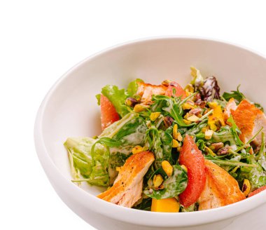 Izgara tavuk, karışık sebze, fındık ve canlı narenciye içeren taze bir salata. Yemek pürüzsüz beyaz bir kasede sunuluyor. Renkli malzemeleri vurguluyor. Besleyici bir yemek için mükemmel..