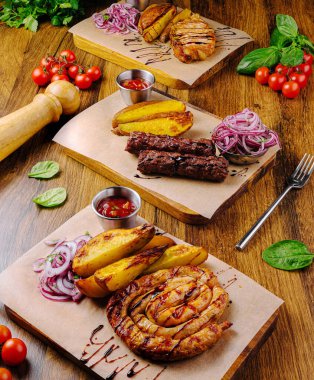 Birkaç tabak et ızgarası, kızarmış patates ve taze sebze. Yemek canlı renklere sahiptir ve tatmin edici bir yemek deneyimi için idealdir..