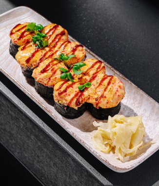 Soslu ve taze otlarla süslenmiş ızgara suşi parçalarının yer aldığı bir suşi tabağı. Turşulu zencefilin yanında servis edilen bu yemek, canlı lezzet ve dokuları yakalar..