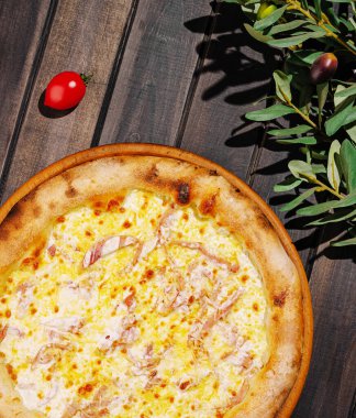 Erimiş peynir ve yumuşak tavuk parçaları ile kaplanmış taze bir pizza kırsal ahşap bir masada oturur. Bir kiraz domatesi ve zeytin dalları, davetkar bir yemek sergiliyor..