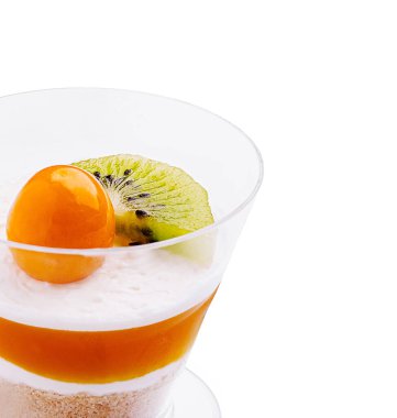 Açık bir cam tabaka içinde sunulan renkli bir tatlı kremalı katmanlar ve canlı meyveler. Üzerinde turuncu bir küre ve çekici bir sunum için bir dilim kivi var..