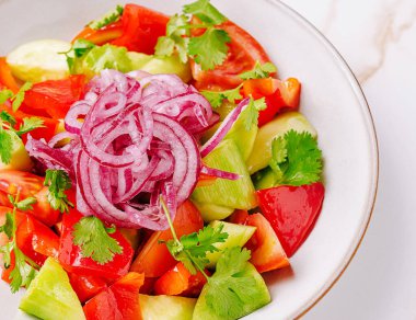 İçinde doğranmış domates, salatalık, dolma biber ve ince dilimlenmiş kırmızı soğan ve kişniş bulunan ferahlatıcı salata dolu bir kase. Hafif bir yemek veya meze için mükemmel..