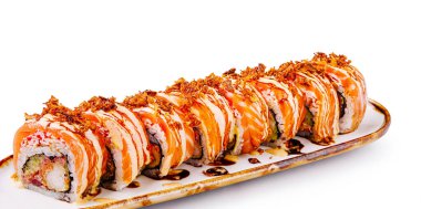 Renkli suşi ruloları üzerinde çıtır çıtır parçalar ve bir sos serpiştirilmiş bir tabakta güzelce düzenlenir. Canlı sunum yemeğin tazeliğini ve ustalıkla hazırlanmasını vurguluyor..