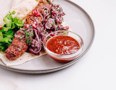 İyi sunulmuş bir kebap tabağında taze soğan ve nar salatası ile kaplanmış lezzetli ızgara et bulunur. Baharatlı sosun bir tarafı yemeğe ekstra tat katıyor..