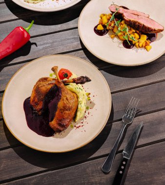 Bir gurme ördek yemeği güzel bir şekilde zengin sos ve kremalı patates püresiyle sunulur. Dekorasyonda renkli süslemeler ve zarif bir ahşap masa, mutfak sanatını gözler önüne seriyor.