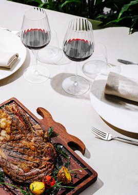 Güzel bir şekilde düzenlenmiş bir yemek masasında renkli sebzelerle çevrili büyük, kavrulmuş bir et parçası yer alır. Yakınlarda oturan iki zarif şarap kadehi davetkar bir yemek deneyimi olduğunu gösteriyor..