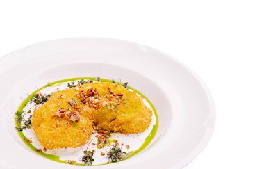 Bir gurme tabağında canlı yeşil bir sosla beyaz bir tabakta sunulan bitkiler ve fındıklarla süslenmiş iki çıtır kızartma sergileniyor. Sunum aşçılık sanatını vurguluyor.