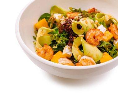 Lezzetli karides, kremalı avokado ve karışık yeşilliklerden oluşan bir yatağa yerleştirilmiş çam fıstığıyla süslenmiş tatlı mango parçaları içeren canlı bir salata..