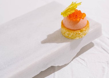 Narin bir tatlı parlak ve çıtır çıtır bir tabanın tepesinde havadar bir köpük sergiliyor. Yaratılışta, minimalist mermer zemin üzerine kurulmuş renkli havyar benzeri malzemeler ve dekoratif bir garnitür yer alıyor..