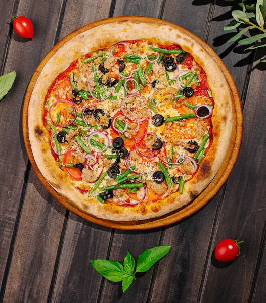 Bu resimde taze bir pizza sergileniyor. Canlı sebzeler ve lezzetli etle dolu, ahşap bir masaya yerleştirilmiş. Taze otlar ve kiraz domatesleri tabağa eşlik ederek, iştah açıcı bir görüntü oluşturur..