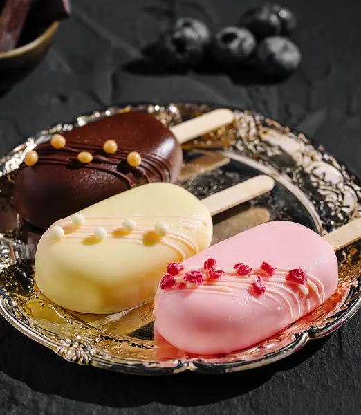 Süslü bir tabakta sanatsal olarak üç renkli dondurma var. Pops farklı tatlar ve malzemeler sunar, bu lezzetli tatlı sunumuna görsel cazibe katar..