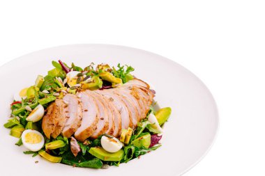 Dilimlenmiş tavuk göğsü ve yarım haşlanmış yumurta içeren taze salata, yeşillik ve sebzelerle süslenmiş. Temiz beyaz bir tabakta servis edilmiş, canlı renkler ve dokular sergiliyor..