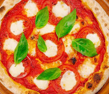 Domates sosu, taze mozzarella ve canlı fesleğen yapraklarıyla kaplı altın kabuklu lezzetli bir Margherita pizzası fırından çıkar. Yemek sıcaklığı ve tazeliği yayar..