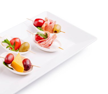 Beyaz bir tabakta küçük aperatiflerden oluşan enfes bir karışım. Şişler peynir, zeytin, kiraz domatesleri ve pişirilmiş etler sunar. Sosyal etkinlik için mükemmeldir..