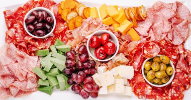 Canlı bir şarküteri tahtası, evde eğlenmek için mükemmel lezzet ve dokuların kombinasyonlarını vurgulayan bir dizi taze et, taze peynir ve renkli meyve sergiliyor..