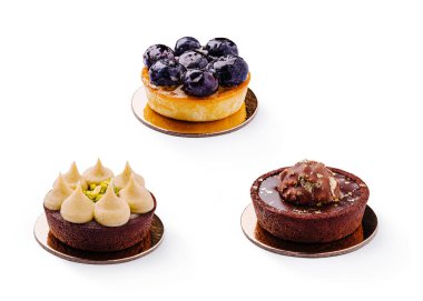 Üç enfes mini tatlıda yaban mersinli tart, çikolatalı tart ve şam fıstıklı kek var. Her tatlı özenle altın tabanlar üzerine sunuluyor, renkli malzemelerini sergiliyorlar..