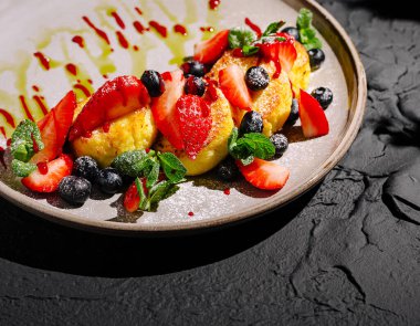 Taze çilek ve yaban mersiniyle kaplanmış, nane yapraklarıyla süslenmiş ve koyu dokulu bir tabakta sunulan renkli tatlı vitrinleri..