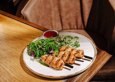 Izgara domuz şişleri ve yanında canlı taze bir salata ve küçük bir kase sos. Samimi ve davetkar bir ortam. Tatmin edici bir yemek için mükemmel..