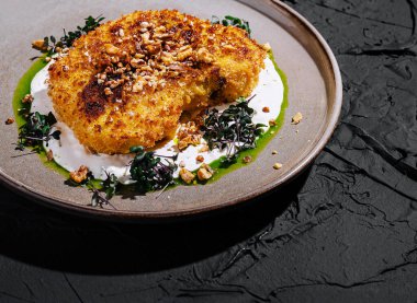 Çıtır bir kızartma tabağı dokulu bir yüzeye kaplanır, yanında da mikroyeşiller ve bir tutam yeşil sos gibi süslenir. Kombinasyon dokuları ve tatları vurgular.