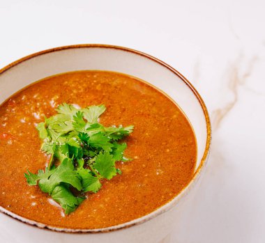 Sıcak bir kase zengin çorbanın üstü canlı kişniş yapraklarıyla kaplıdır. Günün her saatinde sıcak ve davetkar bir yemek sunar..