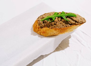 Bir dilim rustik ekmek, taze yeşil bir yaprağın üzerine zengin, lezzetli bir yayılma özelliği taşır. Bu lezzetli ısırık, yemek pişirme sanatını minimalist bir ortamda sergiliyor..