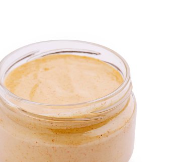 Kremalı fındık ezmesiyle dolu cam bir kavanoz temiz ve beyaz bir zemine dayanır. Pürüzsüz dokusu ve zengin rengi yaymak ve pişirmek için cazibeli doğasını vurgular..